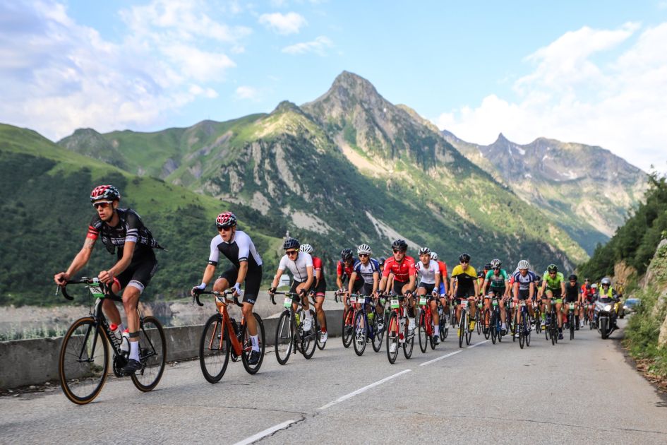 Riders on a mountain bike race in the Alps, with rugged mountain peaks towering in the background.