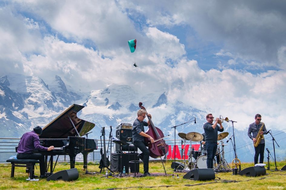 A band of musicians playing at the Cosmo Festival in Chamonix, before a paraglider and mountain views.