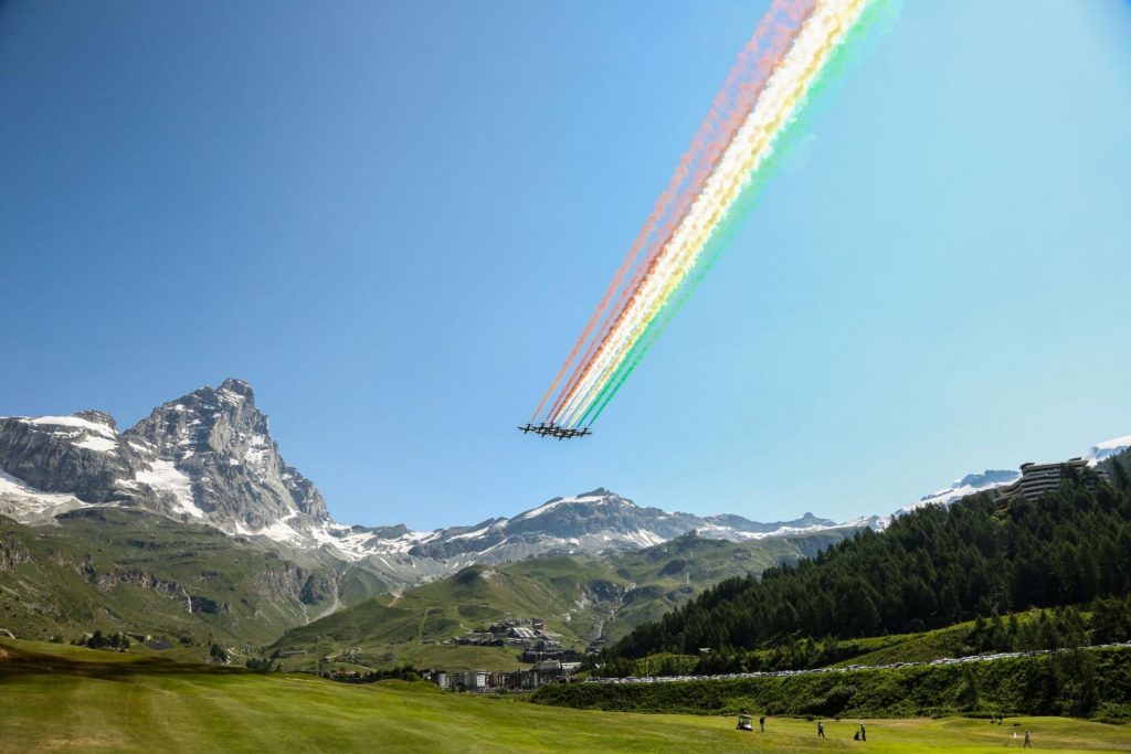 View of Monte Cervino, with planes flying past and golfing in Cervinia below. 