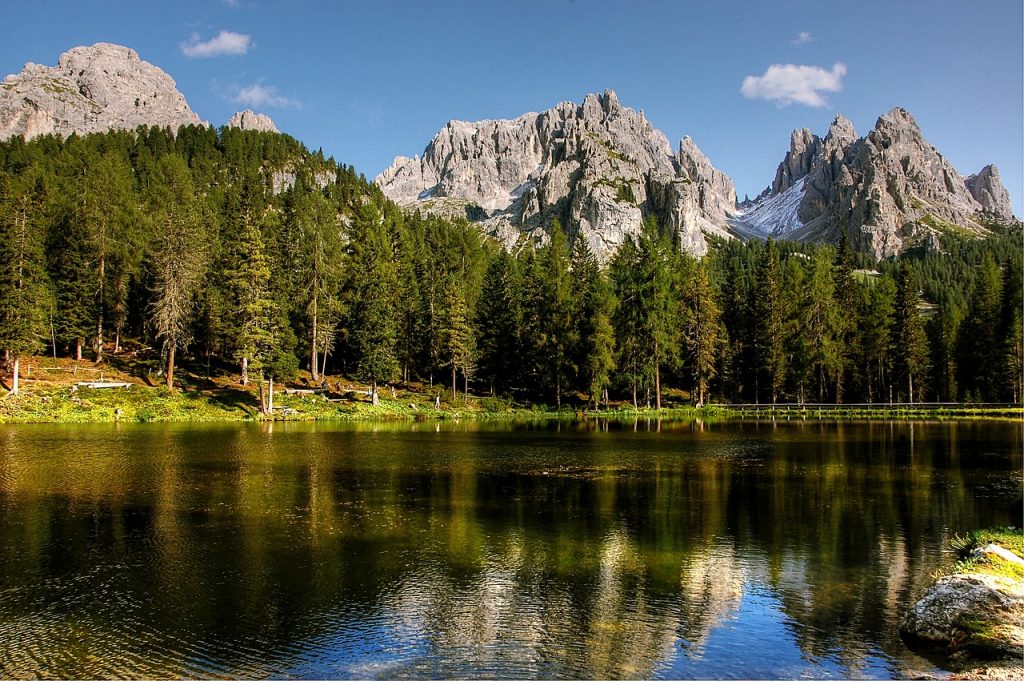 Lake Misurina in the day time with the fir trees and mountain peaks in the background.