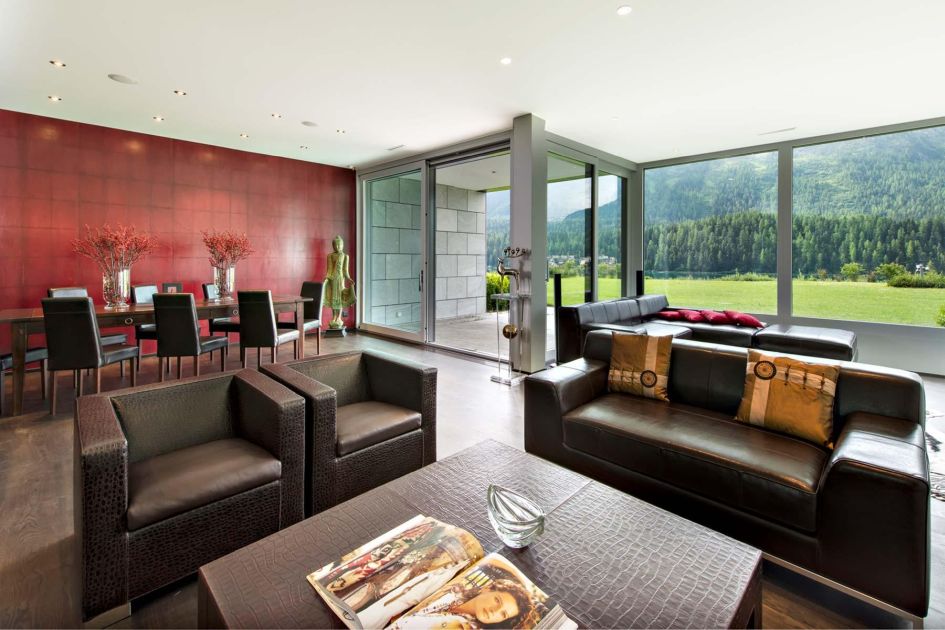 Apartment Snow Garden's main living room adopts a rich, dark design with maroon red walls and chocolate furniture. This space also leads out onto a terrace, through large floor to ceiling picture windows, for better views of Lake St Moritz in autumn.