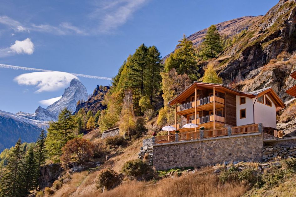 Chalet Gemini is a beautiful freestanding chalet tucked against a beautiful hillside with spectacular views. In addition to the chalet and its hillside, we also see blue skies and the iconic Matterhorn mountain poking through in the distance.