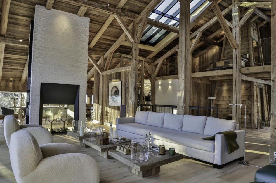 Fermes à la Leonthine is a secluded chalet, located just outside Megève. Within its main living areas, pictured, we see a sofa area, sitting under high vaulted ceilings and exposed beams, all around the central fireplace.