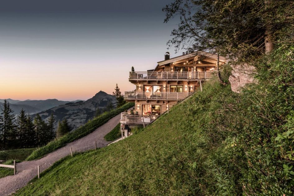 Hahnennkam Lodge sits in a hillside position above the summer resort of Kitzbühel, looking out to views of the sun setting over the mountain landscape and beyond.