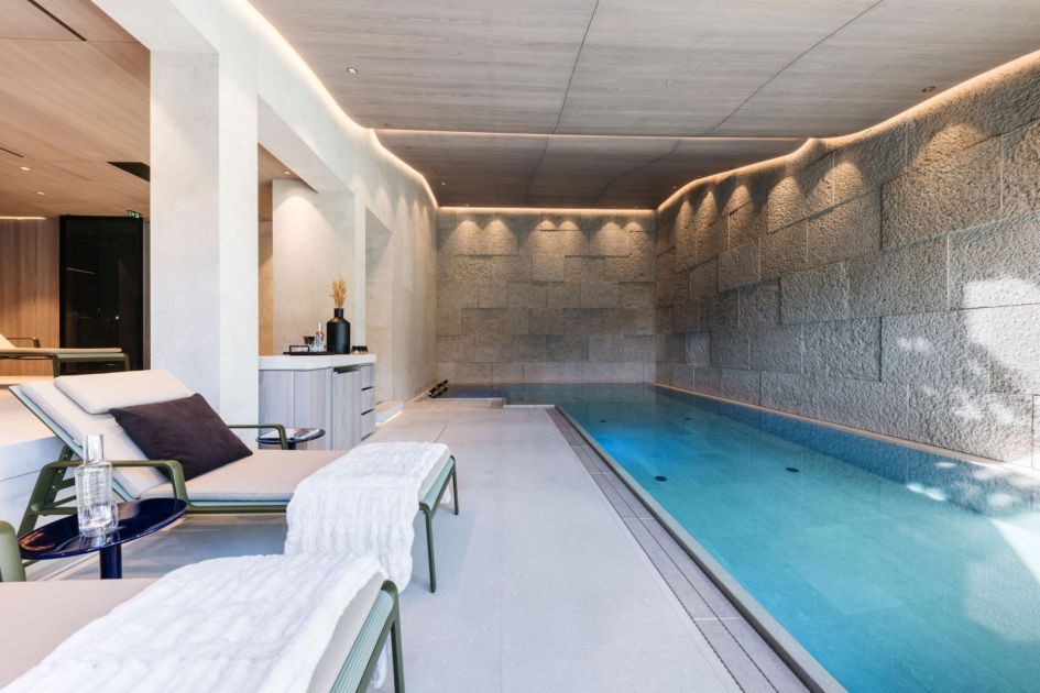 Le Chalet's serene swimming pool hugs the right side of this image, next to the exposed stone walls. Loungers and tables towards the left offer an ideal spot to rest, once you've finished a leisurely swim.