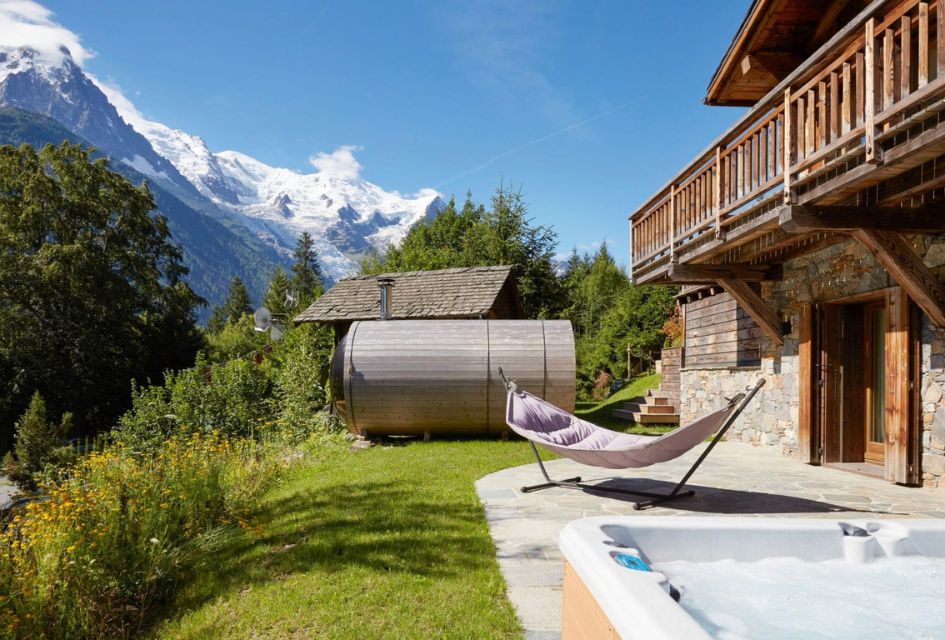 Part of the outdoor space at Eco Lodge, showcasing the barrel sauna, hot tub, and a lounging hammock chair, all with a fantastic holiday view of the mountains
