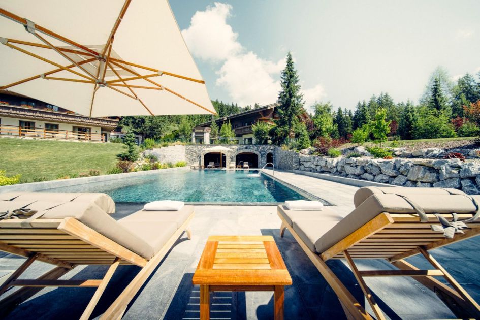 The loungers facing the outdoor pool and exterior of Ultima Crans Montana is the perfect spot to relax under the mountain sun on a large summer chalet holiday!