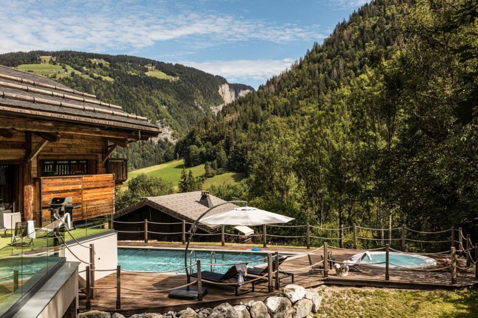 Stunning mountain forest views ahead of the expansive terrace with an outdoor hot tub and indoor/outdoor swimming pool.