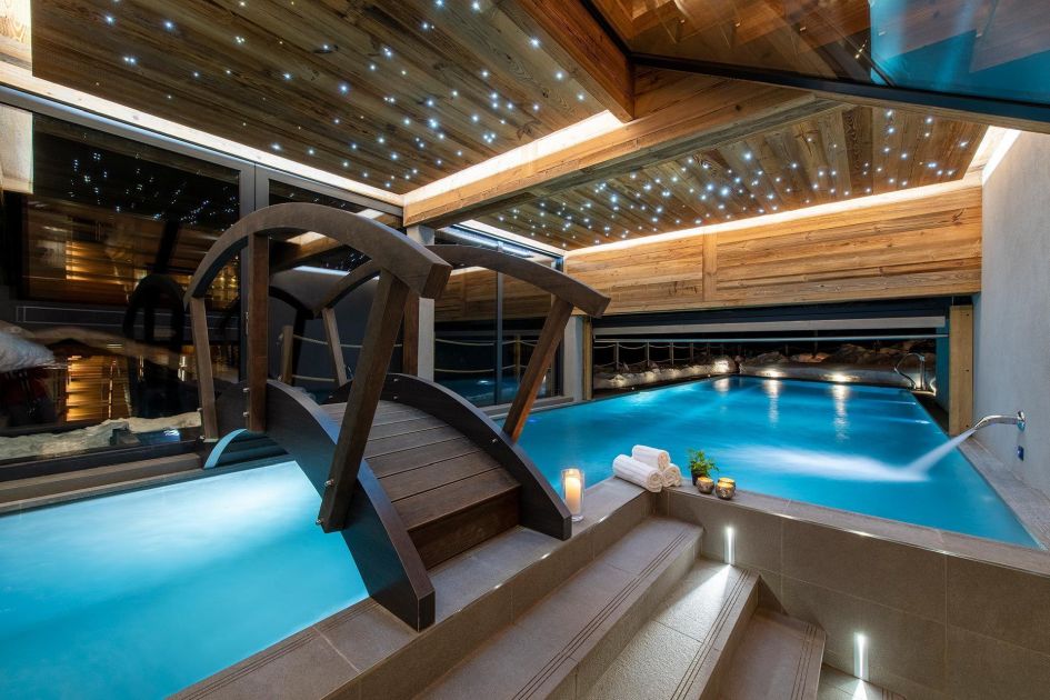 An impressive indoor/outdoor 23m swimming pool with a small bridge over it.